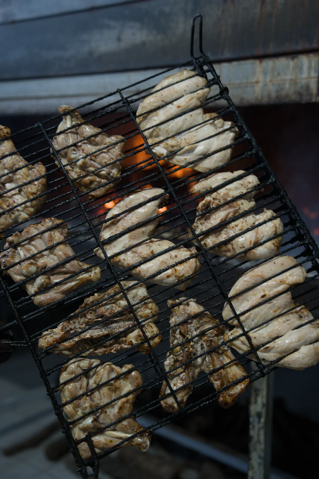 Parrilla con alitas de pollo frente al fuego del asadero